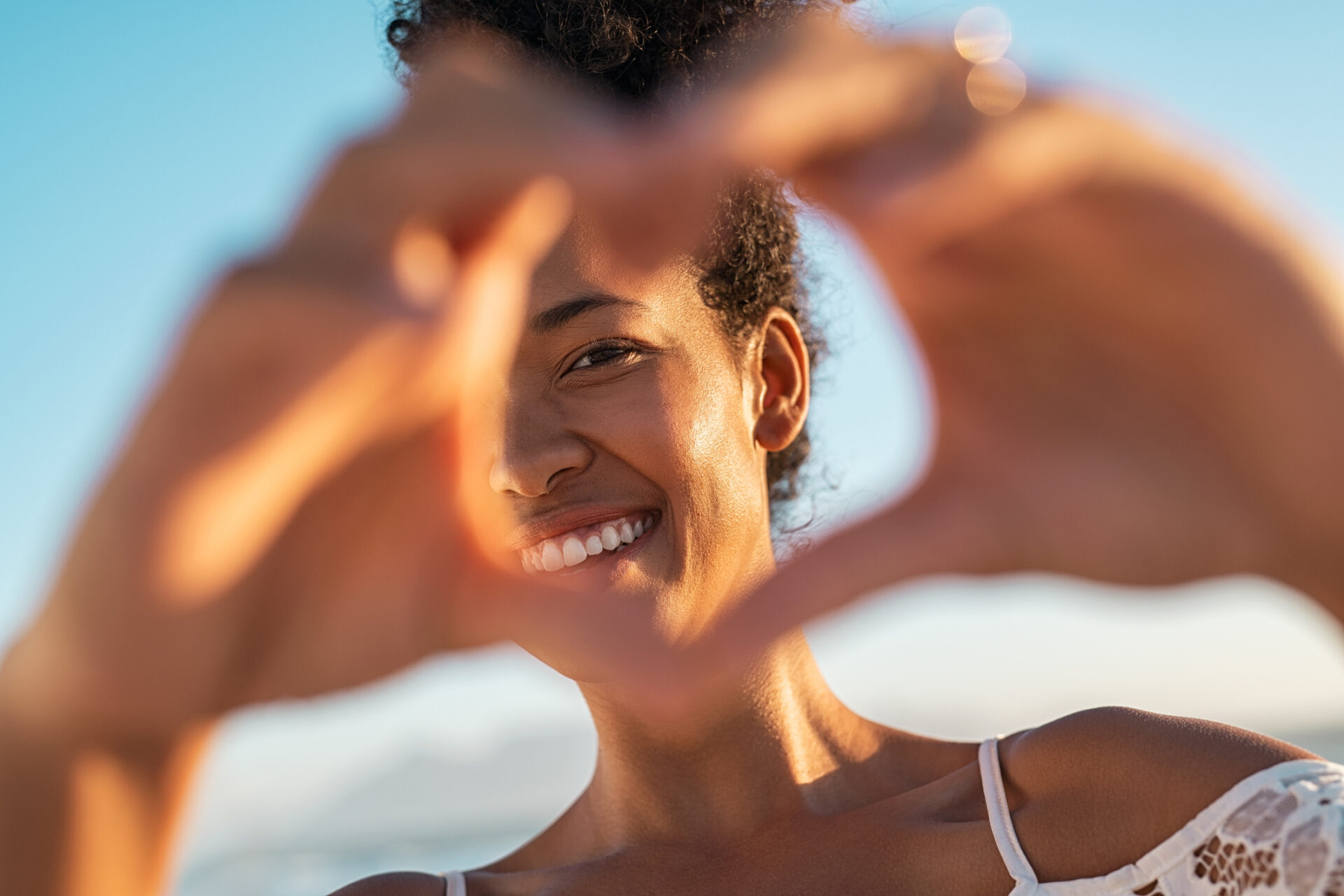 black woman making hand heart at beach during sunset