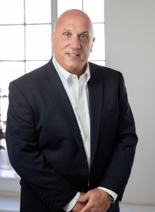 Bank President and CEO, Frank Gaudio, standing in front of a window with hands crossed, smiling.