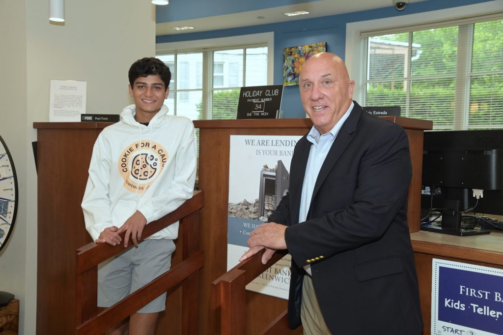 First Bank of Greenwich President & CEO, Frank J. Gaudio, stands at the bank's teller counter with Cookie for a Cause founder Vihaan Kamath.